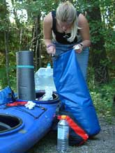 Christine kramt in einem blauen Packsack. Der rotschwarze Sack davor ist schon richtig verschlossen.